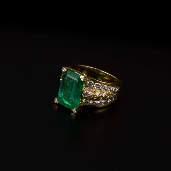 Anillo ancho en oro amarillo y degrade de diamantes talla brillante con un total de 4,10 qts., esmeralda de 4 qts. en verde intenso.